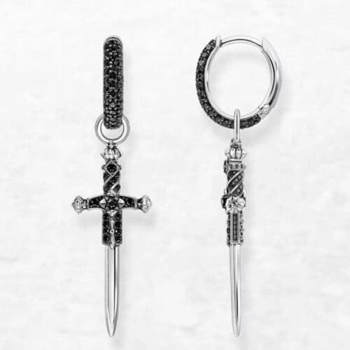 The Black Sword Earrings are silver hoops, each with a hanging ornate cross pendant adorned with small black stones, shown against a light, textured background.
