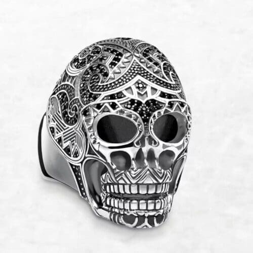 The Maori Skull Ring features intricate black and silver patterns in a detailed, ornate skull design, displayed on a white background.