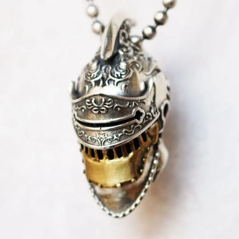 The Roman Knight Helmet Skull Pendant features a medieval helmet design with ornate engravings, a gold-colored visor grill, and hangs from a ball chain.