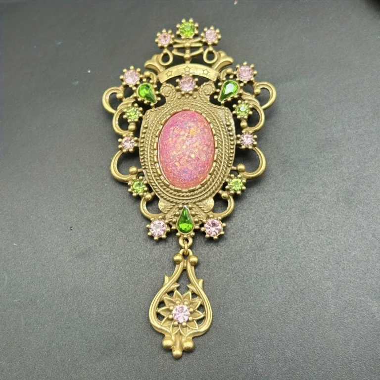 The Baroque Large Vintage Gemstone Brooch features a pink opal-like center, surrounded by pink and green gem accents in ornate gold metalwork, finished with a decorative gold dangle set with a pink gem.