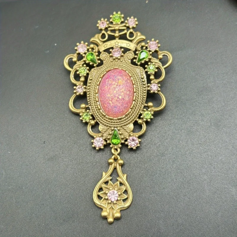 The Baroque Large Vintage Gemstone Brooch features a pink opal-like center, surrounded by pink and green gem accents in ornate gold metalwork, finished with a decorative gold dangle set with a pink gem.