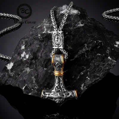 The Thor’s Viking Hammer Amulet Necklace | Norse Mythology Jewellery features silver and gold details with intricate Norse designs, hanging on a thick chain and displayed against a rugged black stone background.