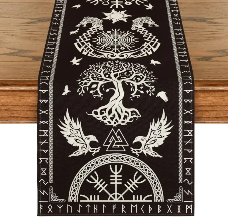 The Viking Linen Table Runner | Nordic Table Décor in black, with white Norse-inspired designs—tree of life, ravens, wolves, runes, and geometric patterns—is displayed on a wooden table.
