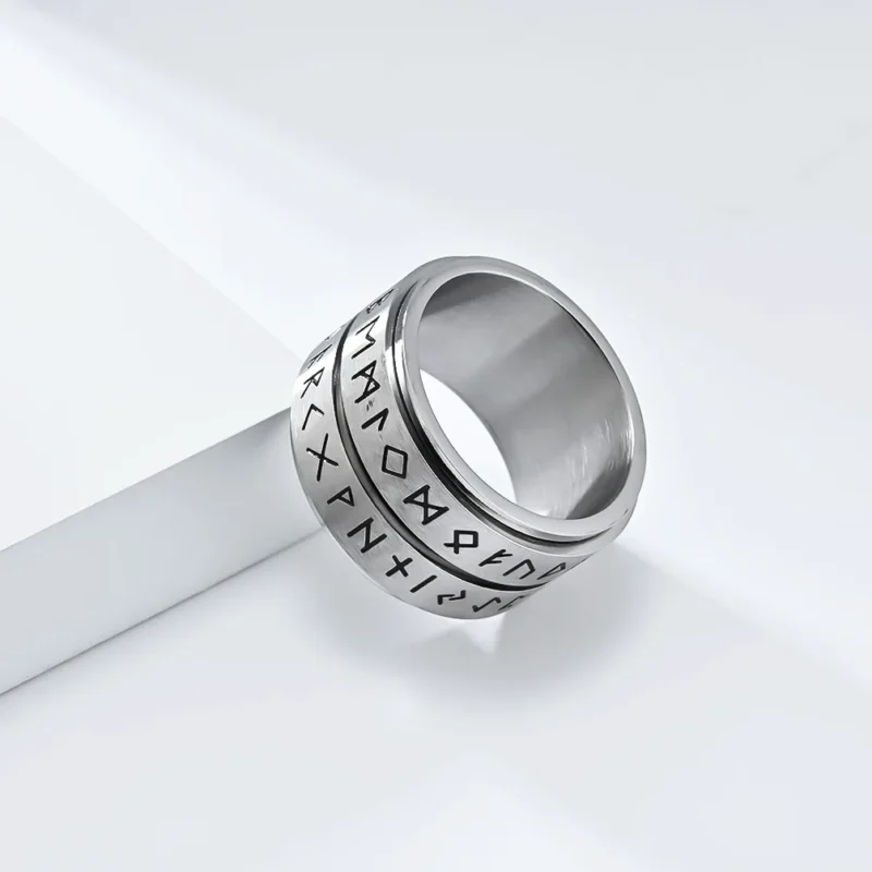 The Nordic Viking Rune Spinner Ring is a wide, silver-colored ring with a worn, textured finish and two rows of engraved runic symbols around its exterior.