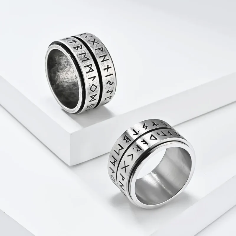 The Nordic Viking Rune Spinner Ring is a wide, silver-colored ring with a worn, textured finish and two rows of engraved runic symbols around its exterior.